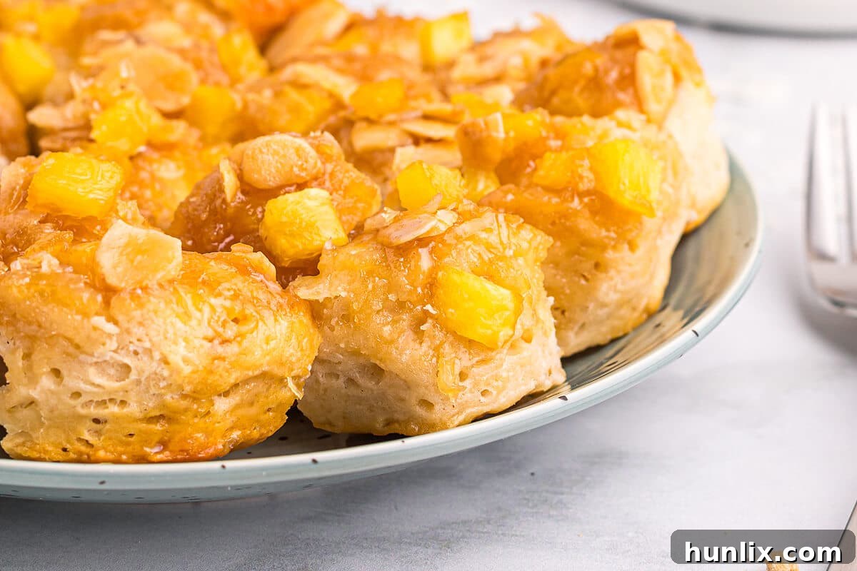 Pineapple Paradise Sticky Buns with Coconut Caramel Sauce 9 A close-up of a single pineapple sticky bun on a white plate, showcasing the glistening coconut caramel, pineapple pieces, and a few almonds, ready to be enjoyed.