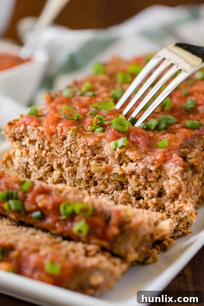 A close-up of a slice of Mexican Meatloaf on a plate, with a fork ready to enjoy the succulent, cheesy goodness.