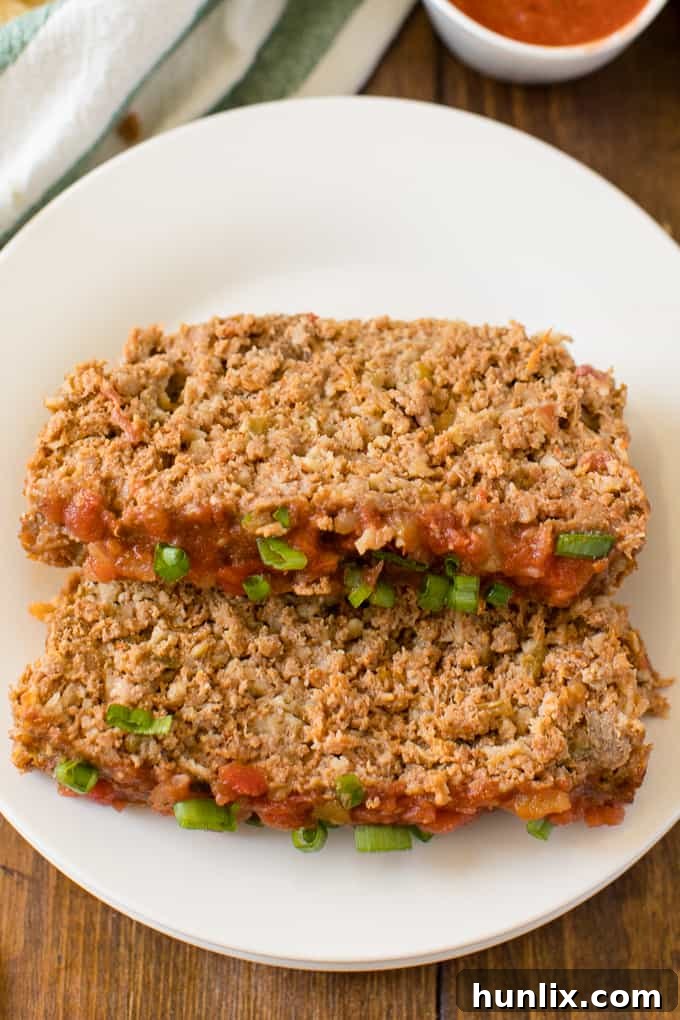 A close-up photo of a plate with multiple slices of Mexican Meatloaf, garnished with fresh green onions and ready to eat.