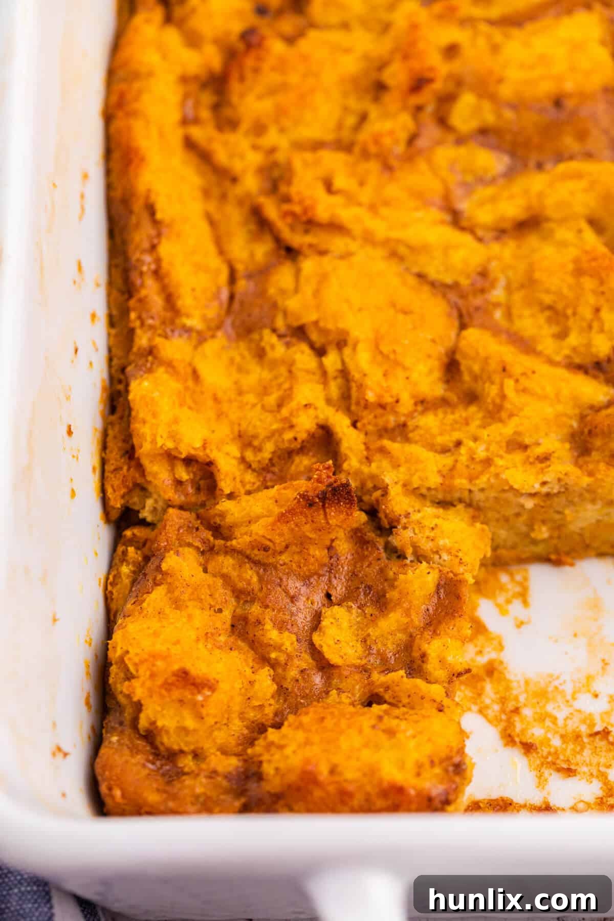 Pumpkin gingerbread pudding in a pan with a piece cut out.