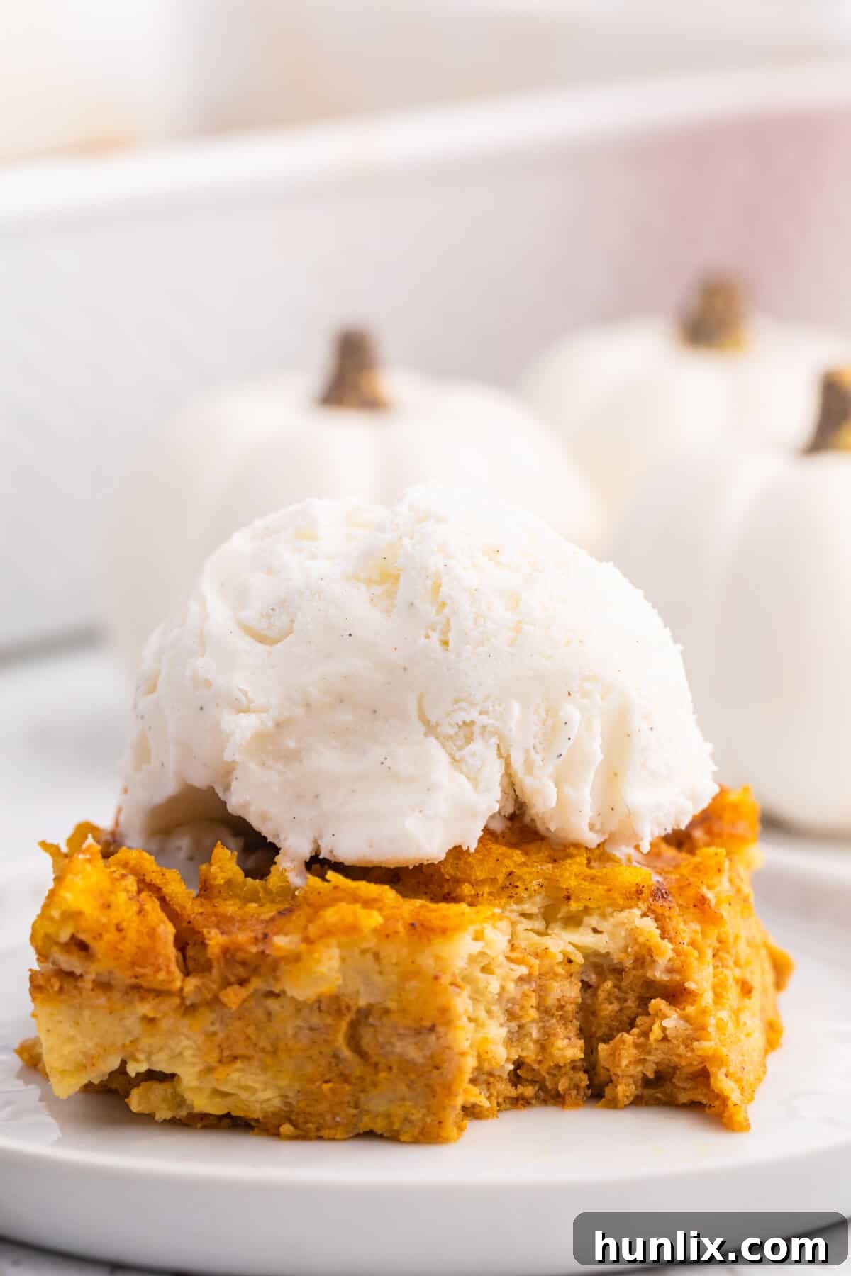 A piece of pumpkin gingerbread pudding on a plate topped with vanilla ice cream.