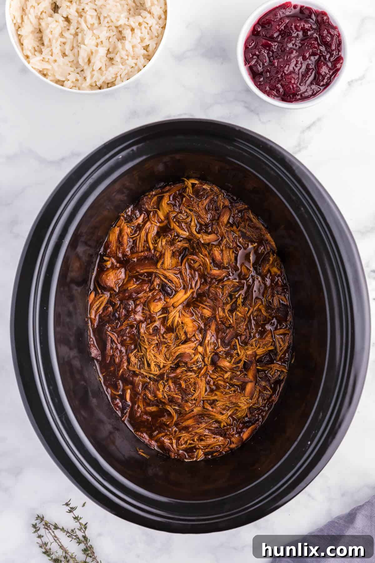 Tender Slow Cooker Cranberry Chicken breasts in a sweet and savory sauce, garnished with fresh thyme. Perfect for easy weeknight meals.