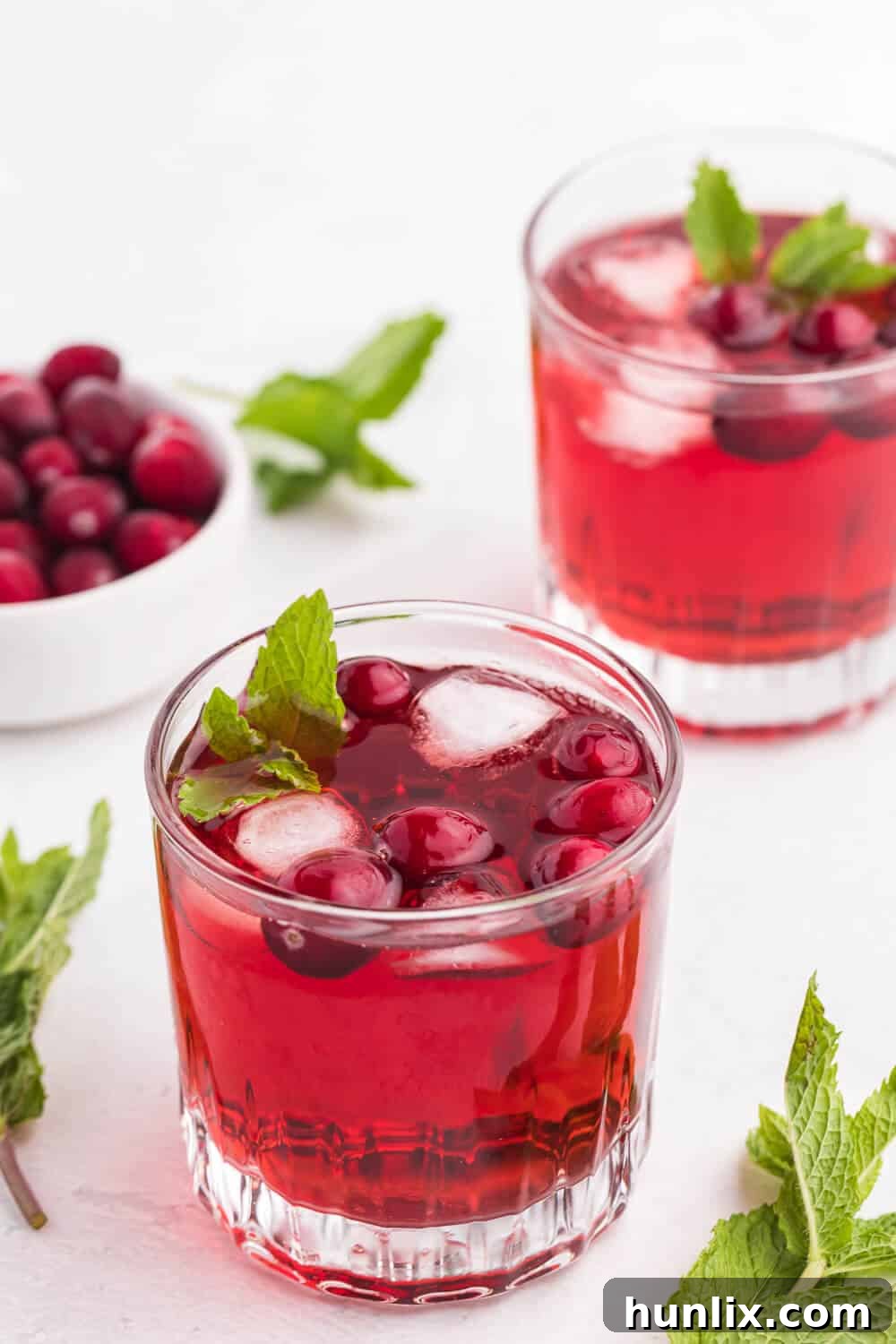 Glasses of sparkling cranberry mint mocktail on a white surface, garnished with fresh mint and cranberries.