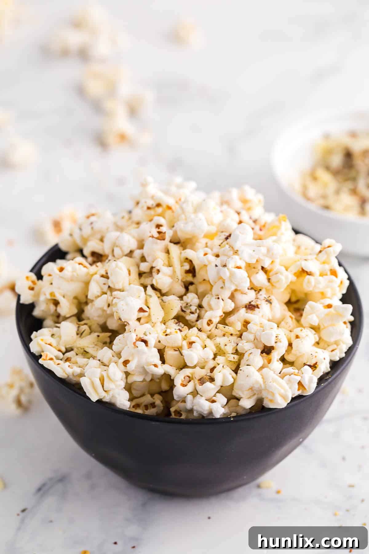 A bowl overflowing with freshly made Pizza Popcorn, garnished with herbs and a sprinkle of red pepper flakes.