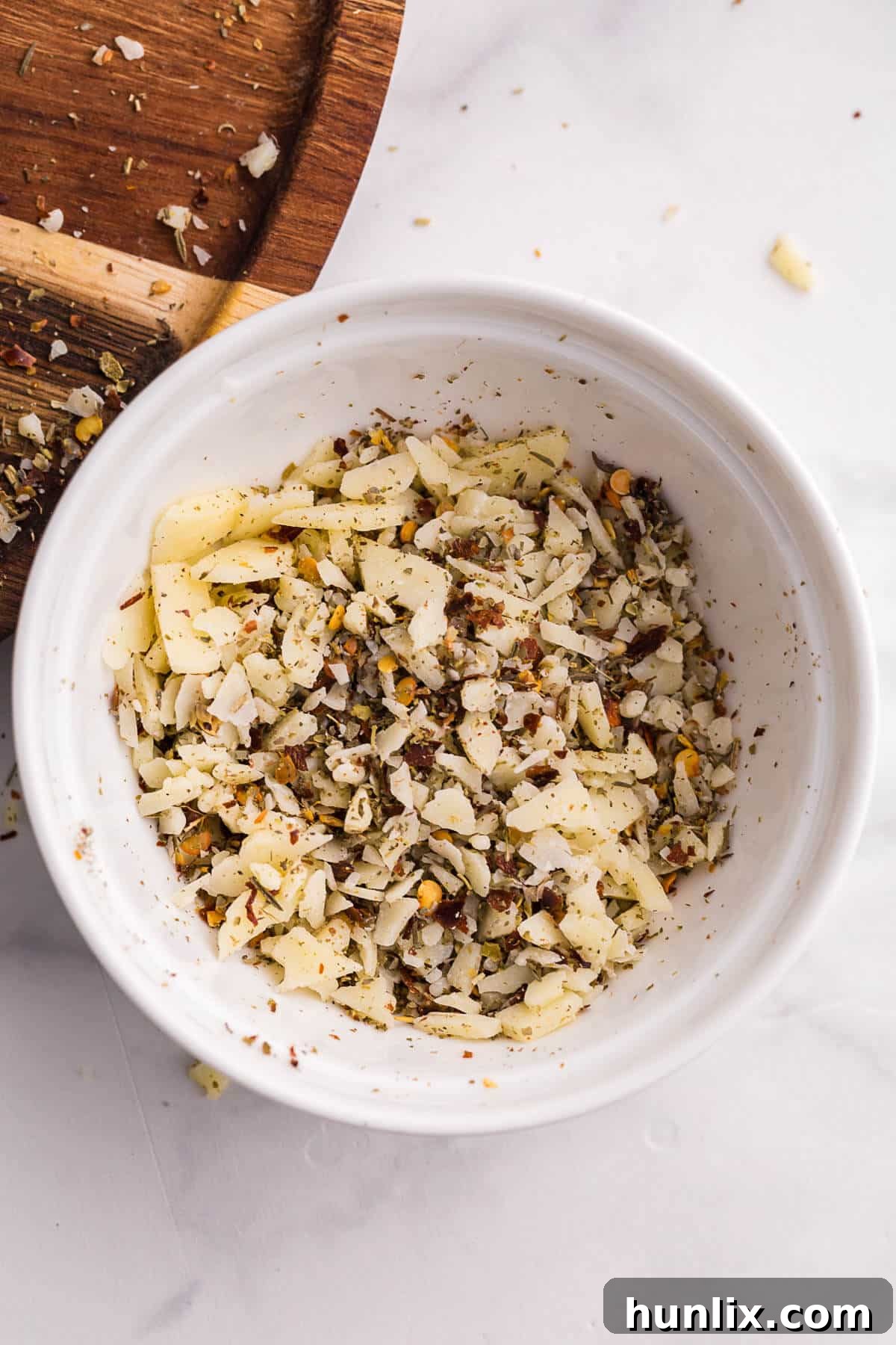 Close-up shot of the simple Pizza Popcorn topping ingredients in separate bowls: grated Parmesan cheese, Italian seasoning, and red pepper flakes, ready to be added to popcorn.