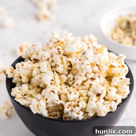 A bowl overflowing with freshly made Pizza Popcorn, garnished with herbs and a sprinkle of red pepper flakes.