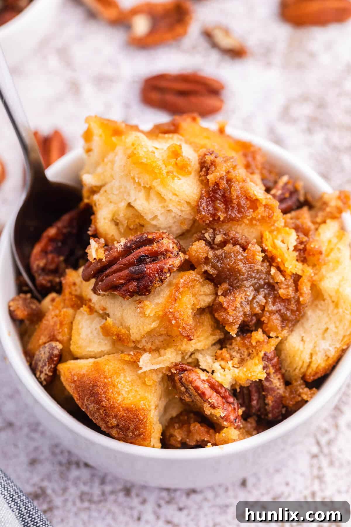 A serving of Pecan butter tart buns in a white bowl with a spoon, highlighting the sticky texture.