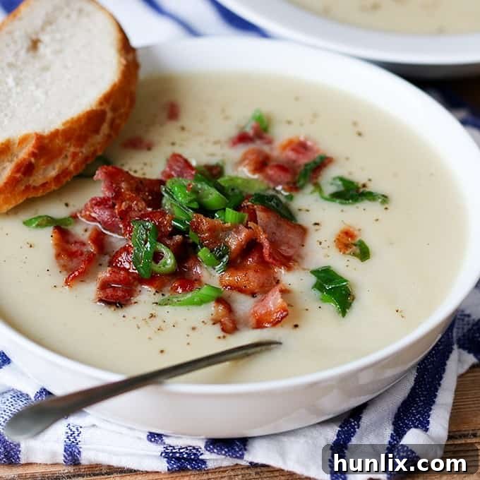 Creamy Cauliflower Bacon Bisque 3 A close-up shot of creamy cauliflower soup in a bowl, with a spoon resting in it and a slice of bread beside it, inviting you to take a bite.