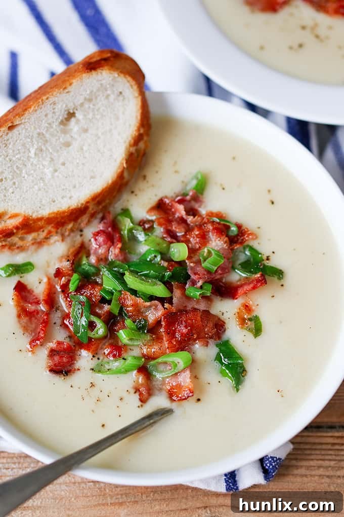 Creamy Cauliflower Bacon Bisque 5 A tall, inviting shot of creamy cauliflower soup, topped with generous crispy bacon and fresh scallions, with a spoon ready to dive in and a rustic bread slice.