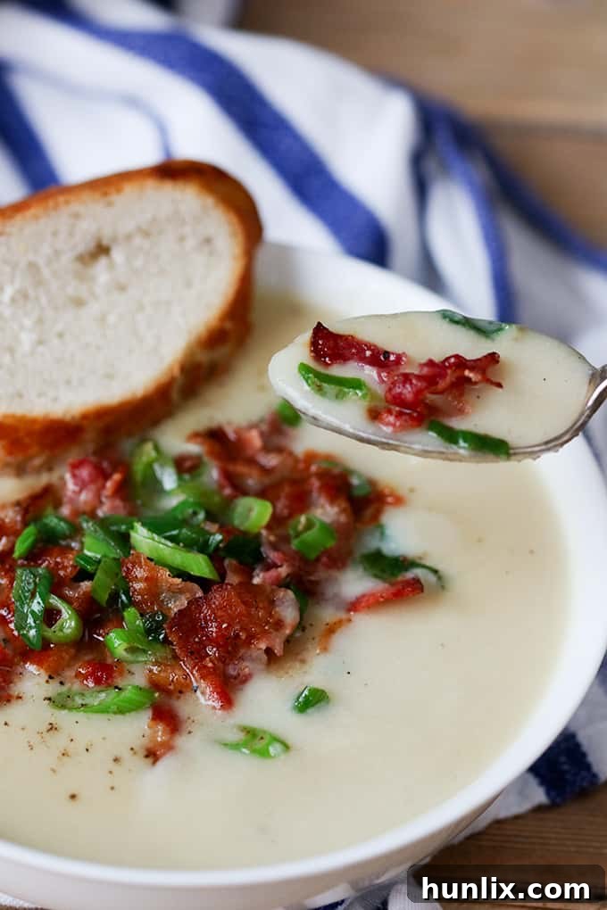 Creamy Cauliflower Bacon Bisque 7 A close-up of a spoon lifting creamy cauliflower soup adorned with crispy bacon bits, showcasing the rich texture and appealing garnish.