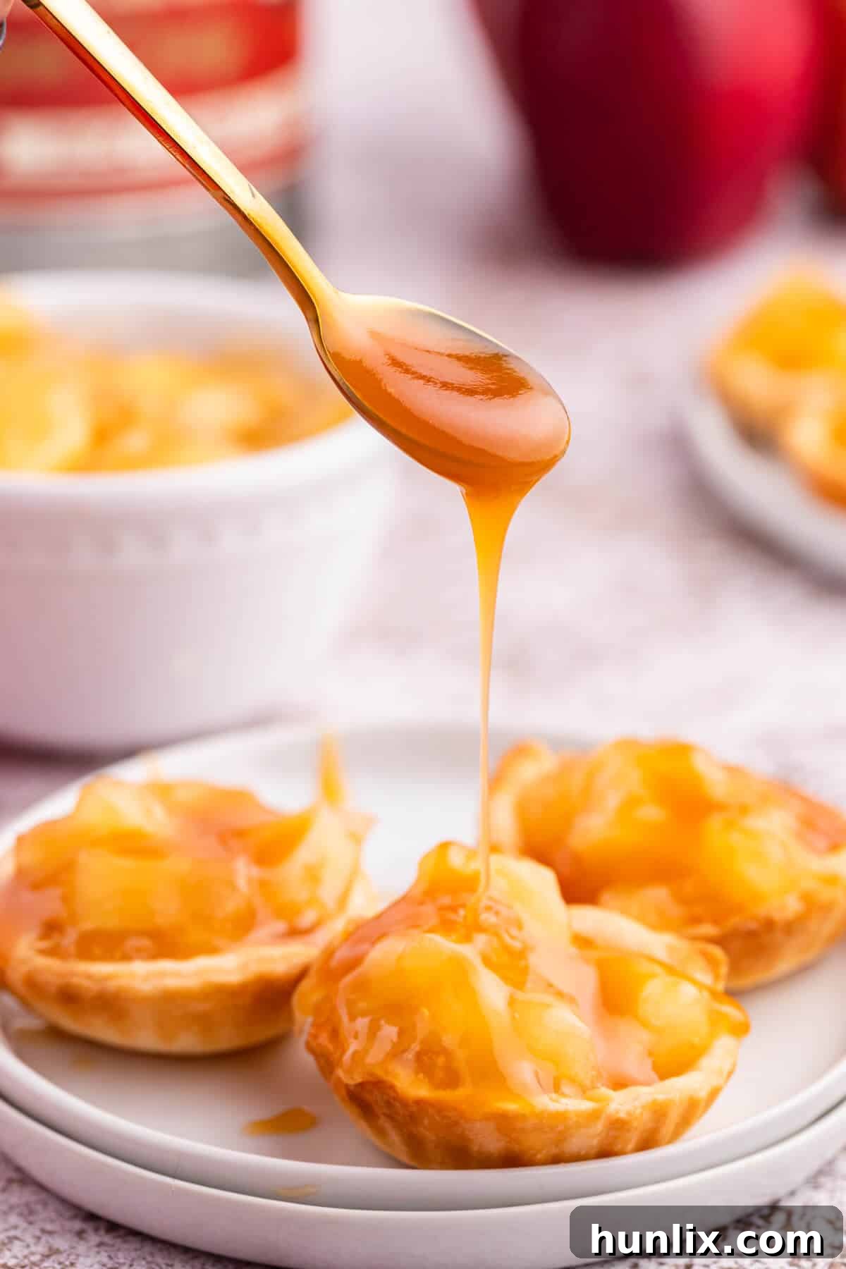 A spoon delicately drizzling caramel sauce over a freshly baked caramel apple tart.