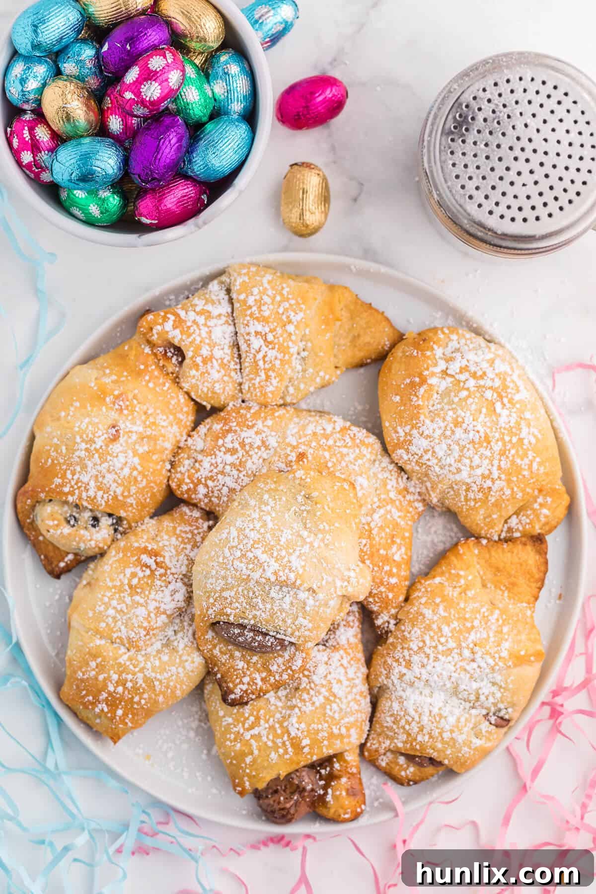 Golden brown Easter egg stuffed crescent rolls dusted with powdered sugar, served on a white plate, showcasing a gooey melted chocolate center.