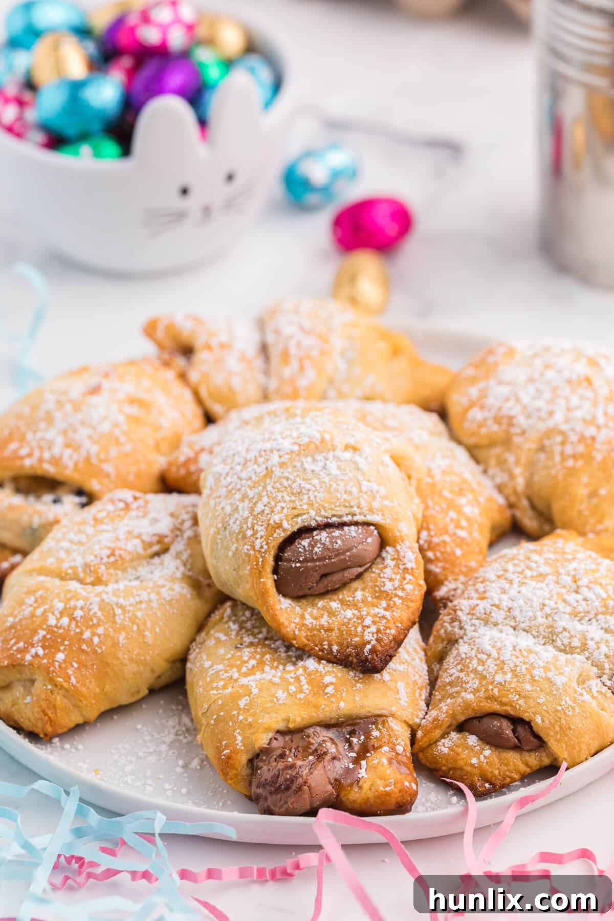 A cluster of golden Easter egg stuffed crescent rolls, lightly dusted with powdered sugar, arranged on a rustic white plate.