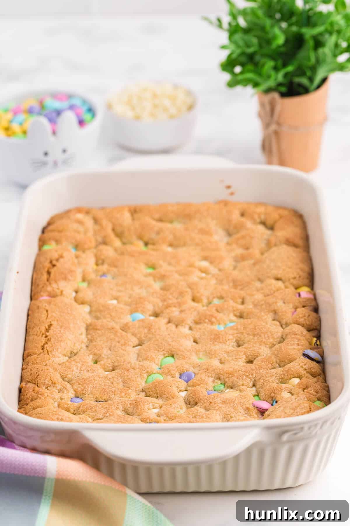 Spring Bloom Cookie Bars 2 A baking pan filled with freshly baked Spring Cookie Bars, showcasing their golden-brown edges, chewy texture, and a scattering of colorful pastel M&Ms and white chocolate chips.