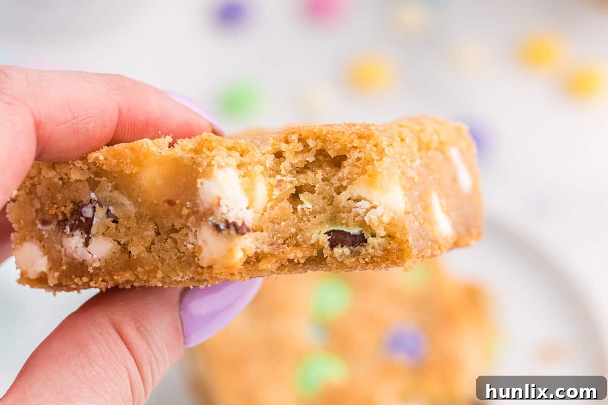Spring Bloom Cookie Bars 6 A hand gently holds a single Spring Cookie Bar, showcasing its perfect size, vibrant M&Ms, and tempting texture.