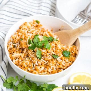 Curried lentil rice in a white bowl with a wooden spoon.