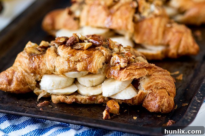 Sticky banana croissants on a baking sheet after topping with frangipane and nuts.