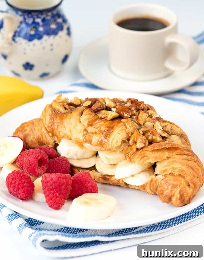 A close-up of a sticky banana croissant with crushed nuts, served on a plate with fresh berries.