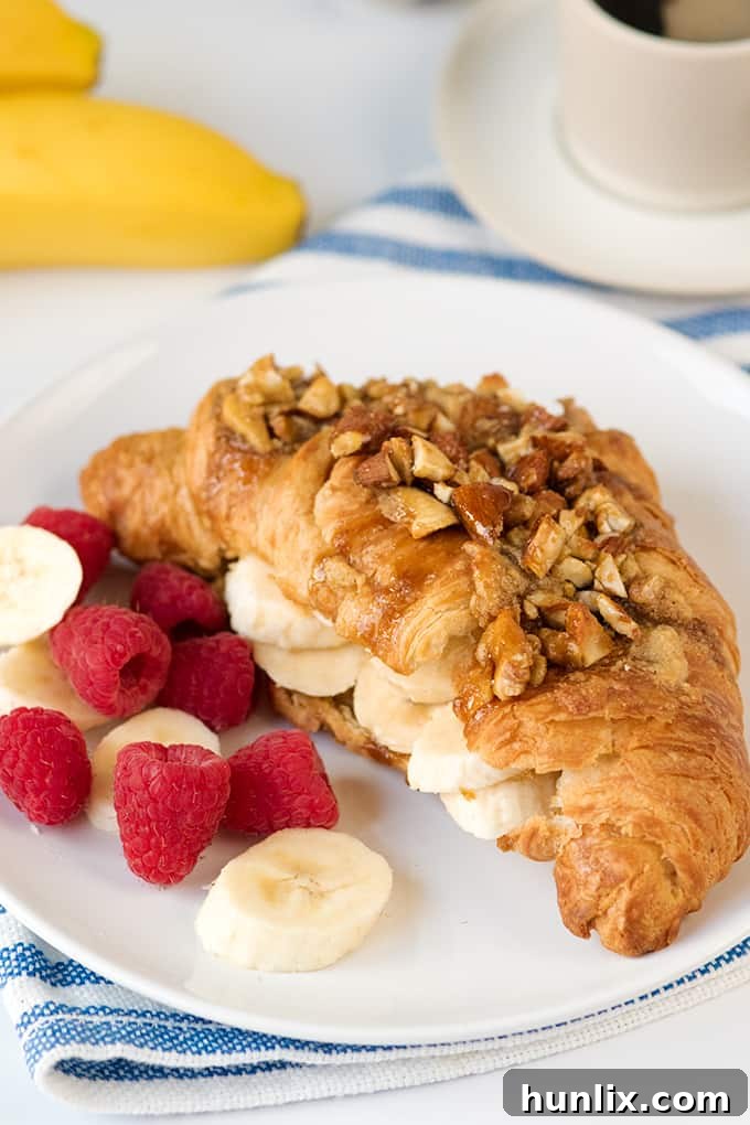 A delicious sticky banana croissant with crushed nuts, garnished with fresh berries and mint.