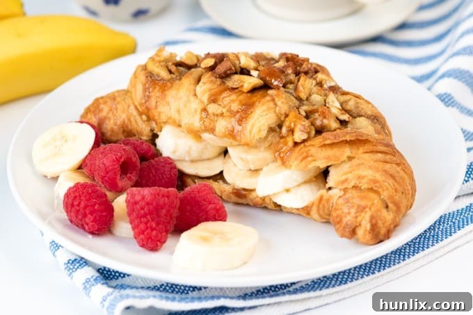 Sticky banana croissant on a white plate with fresh bananas and raspberries.