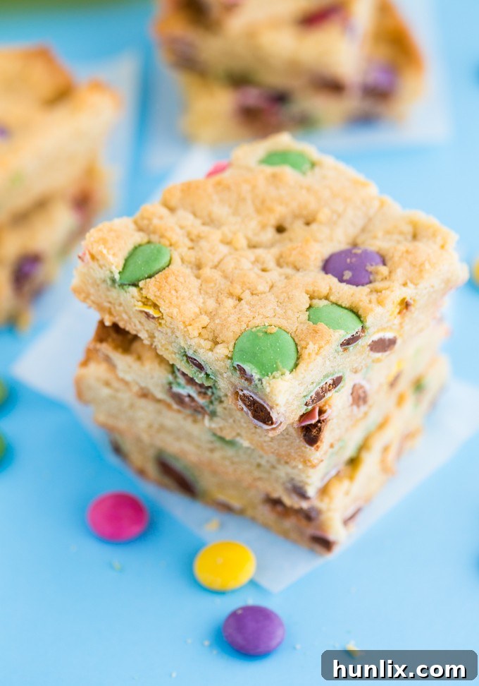 A stack of Smarties Blondies, showcasing their thick, fudgy center and the generous amount of candy-coated chocolates.