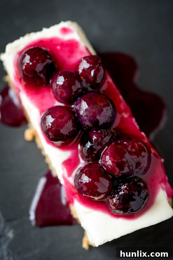Close-up of a single blueberry lemon cheesecake bar on a black surface, highlighting its layers.