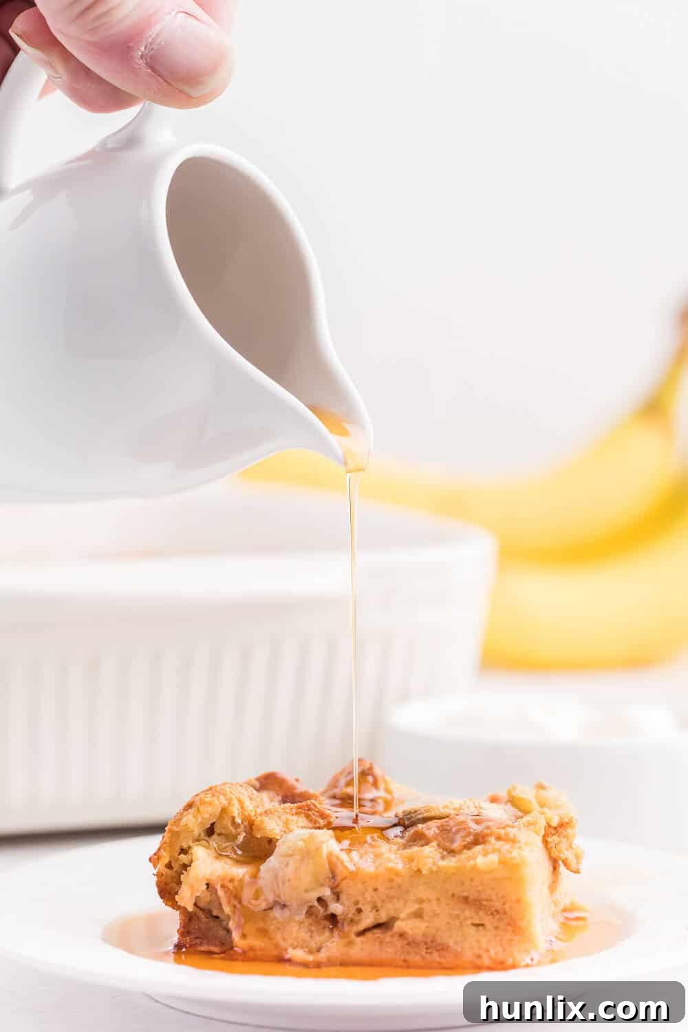 Maple syrup being drizzled over a slice of Banana Bread Breakfast Casserole on a plate.
