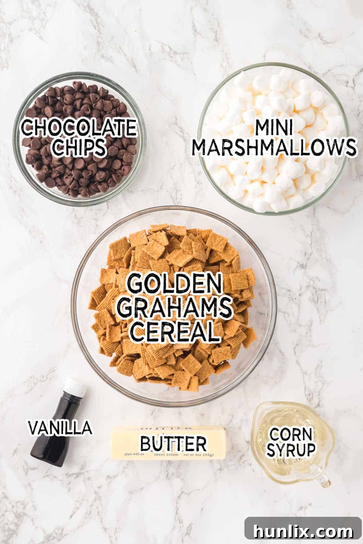 A flat lay photograph showcasing all the ingredients for indoor s'mores on a white marble background.