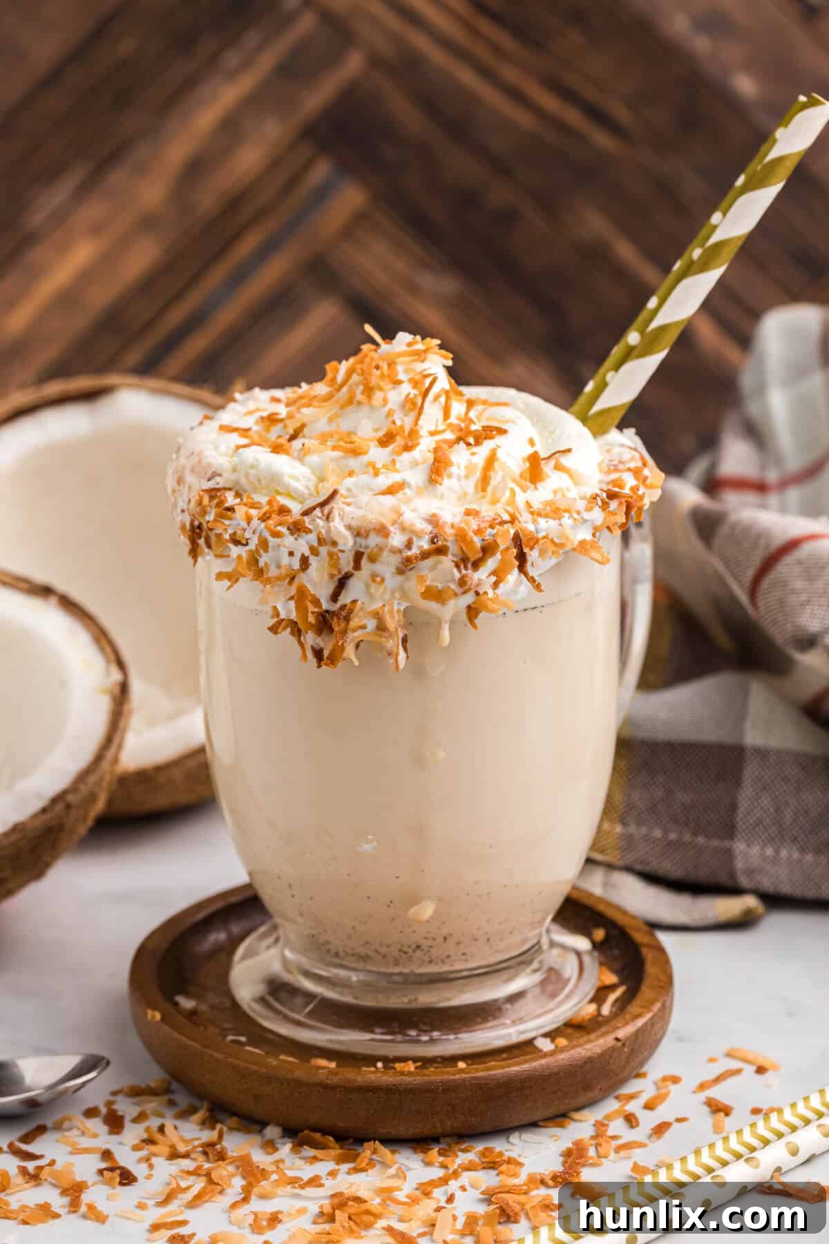 Coconut coffee milkshake on a wooden coaster, garnished with whipped cream and toasted coconut, ready to be enjoyed.