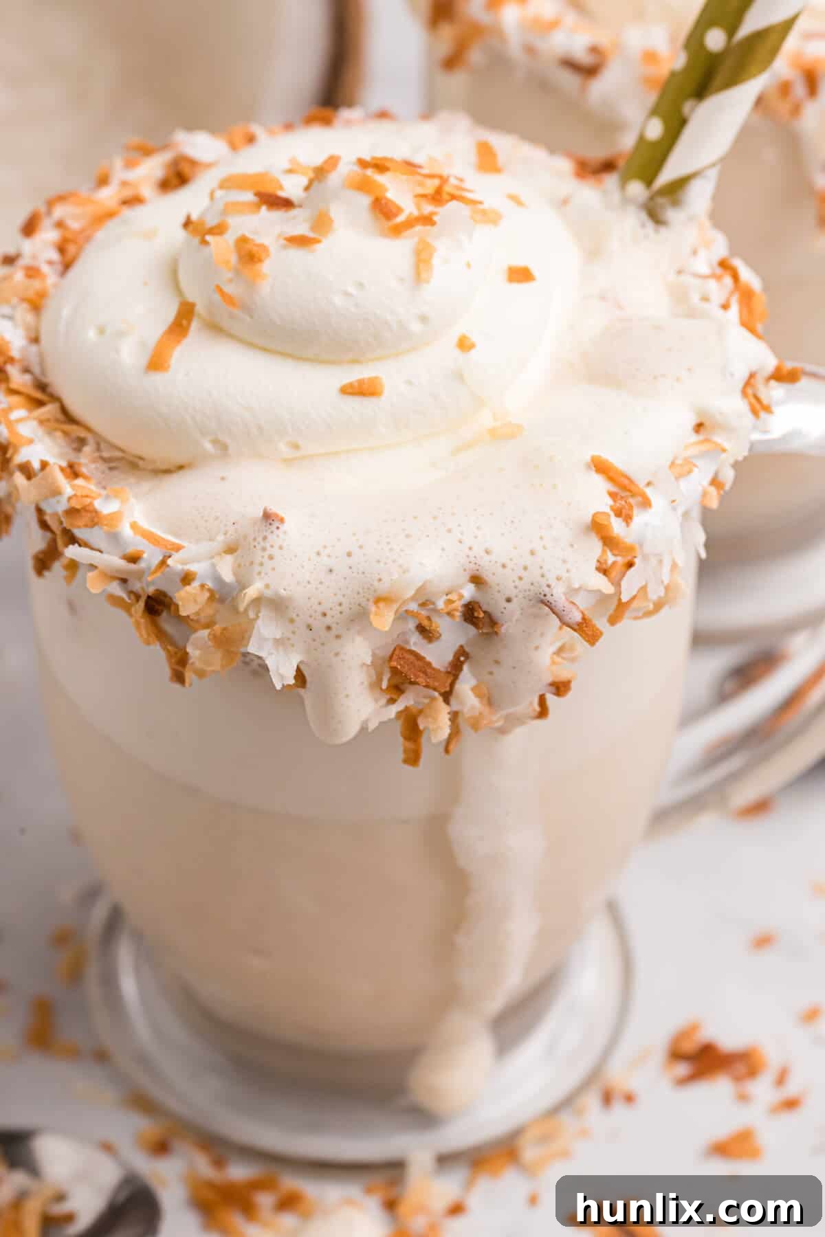 A glass of Coconut Coffee Milkshake with a visible drip on the side, highlighting its creamy texture, on a simple background.