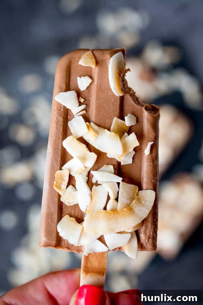 A hand holding a toasted coconut fudgsicle with a bite out of the top.