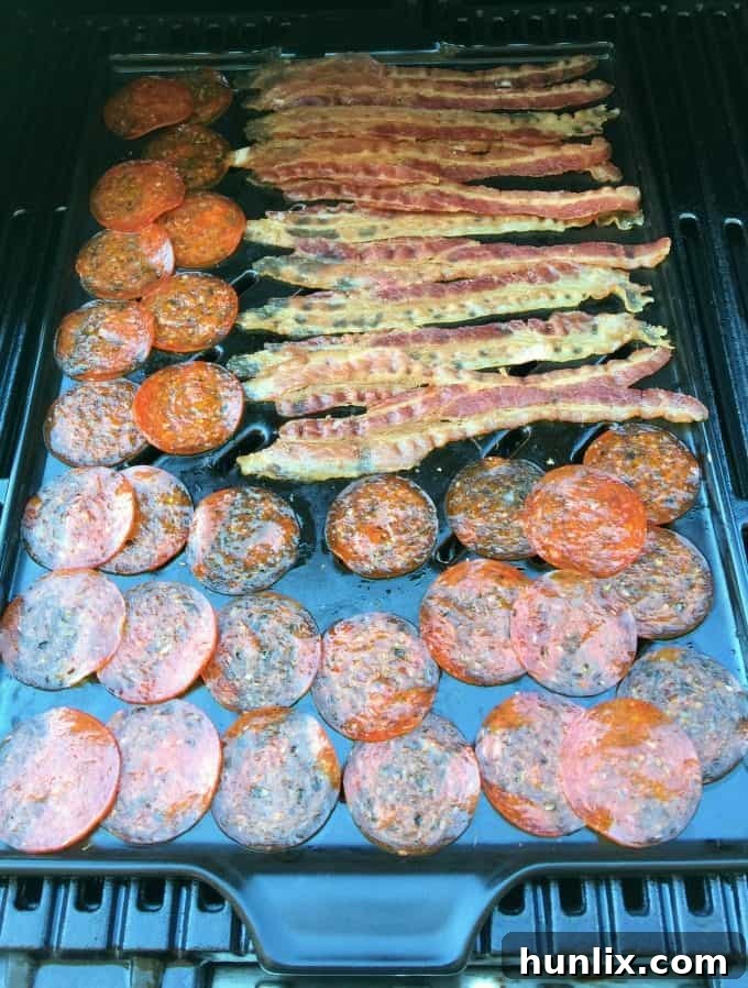 Bacon and pepperoni slices being heated on the grill, ready to top the Deluxe Pizza Burgers.