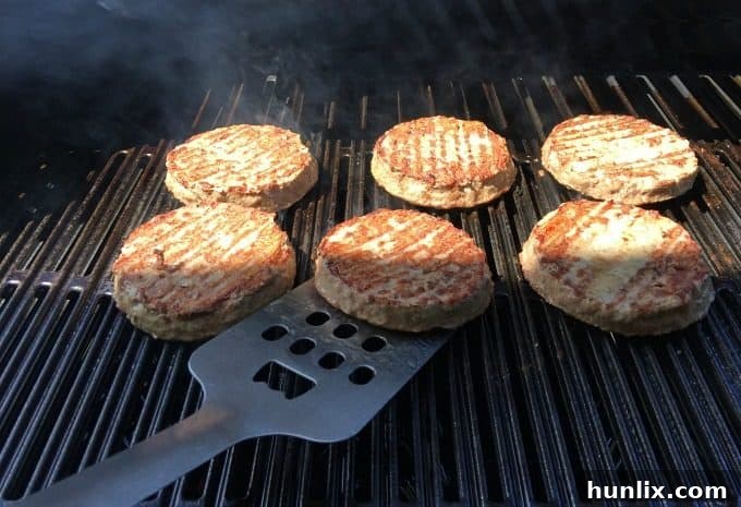 Thick Angus beef burgers sizzling on the grill, forming the base of the Deluxe Pizza Burgers.