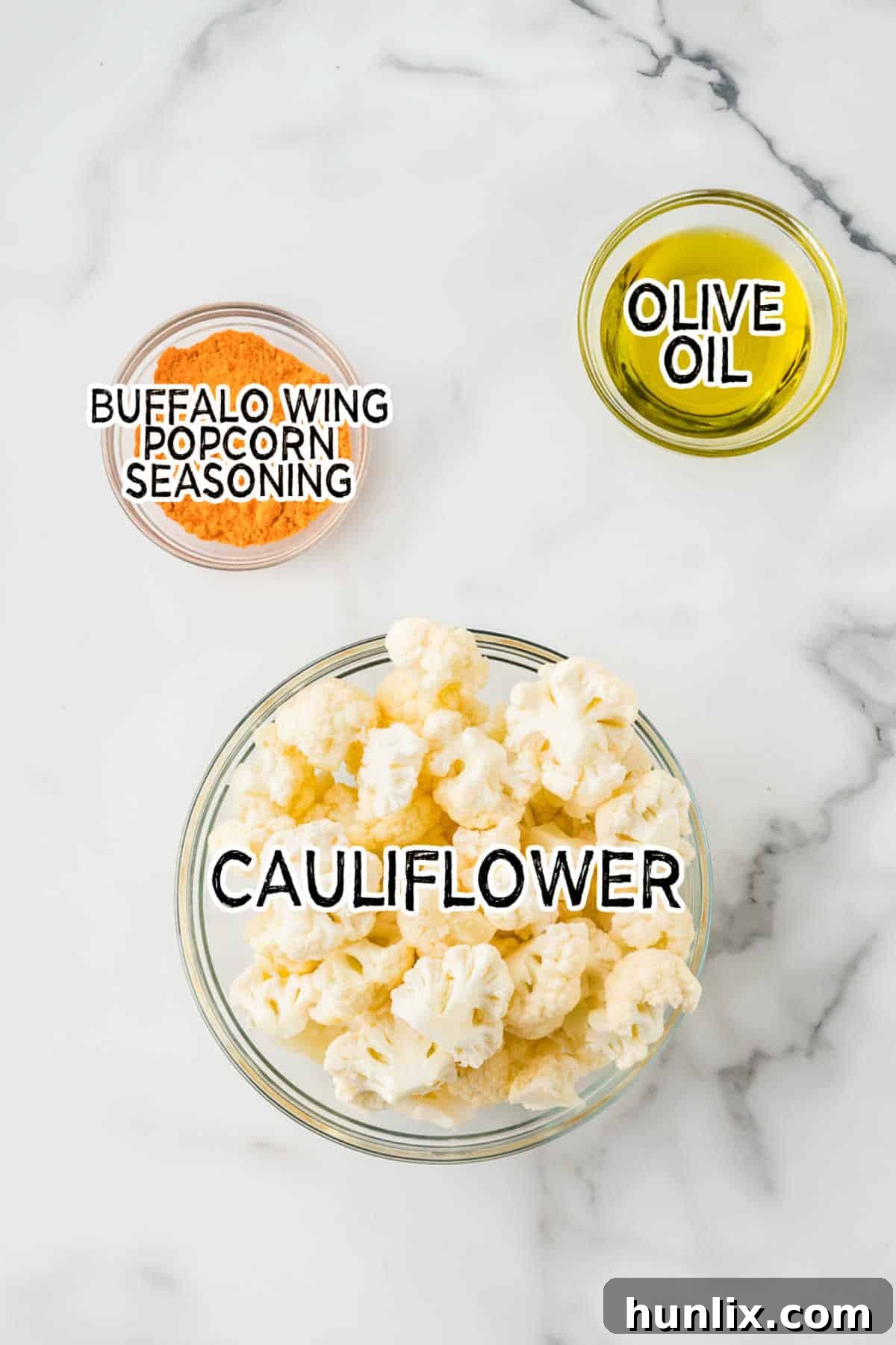 Spicy Buffalo Popcorn 4 Display of the three main ingredients: a whole head of cauliflower, a bottle of extra virgin olive oil, and a container of buffalo wing popcorn seasoning.