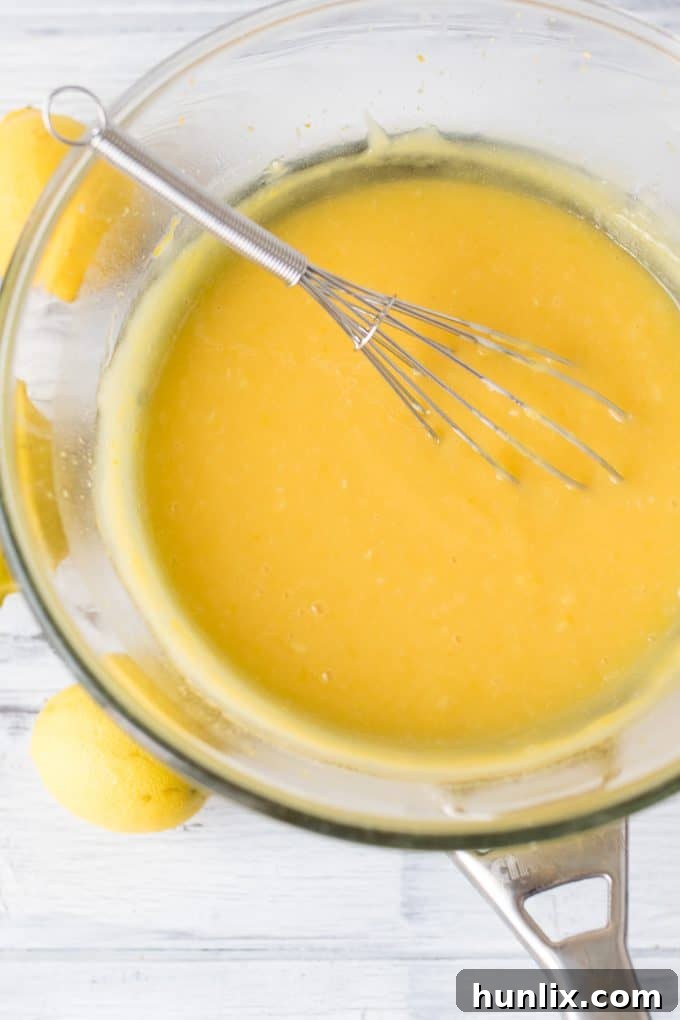 Homemade lemon curd in a glass pot with a whisk.