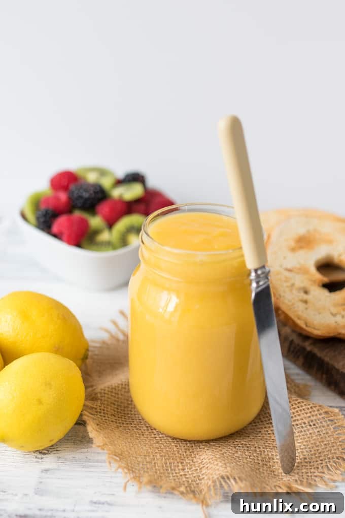 Homemade lemon curd in a glass jar with a butter knife.