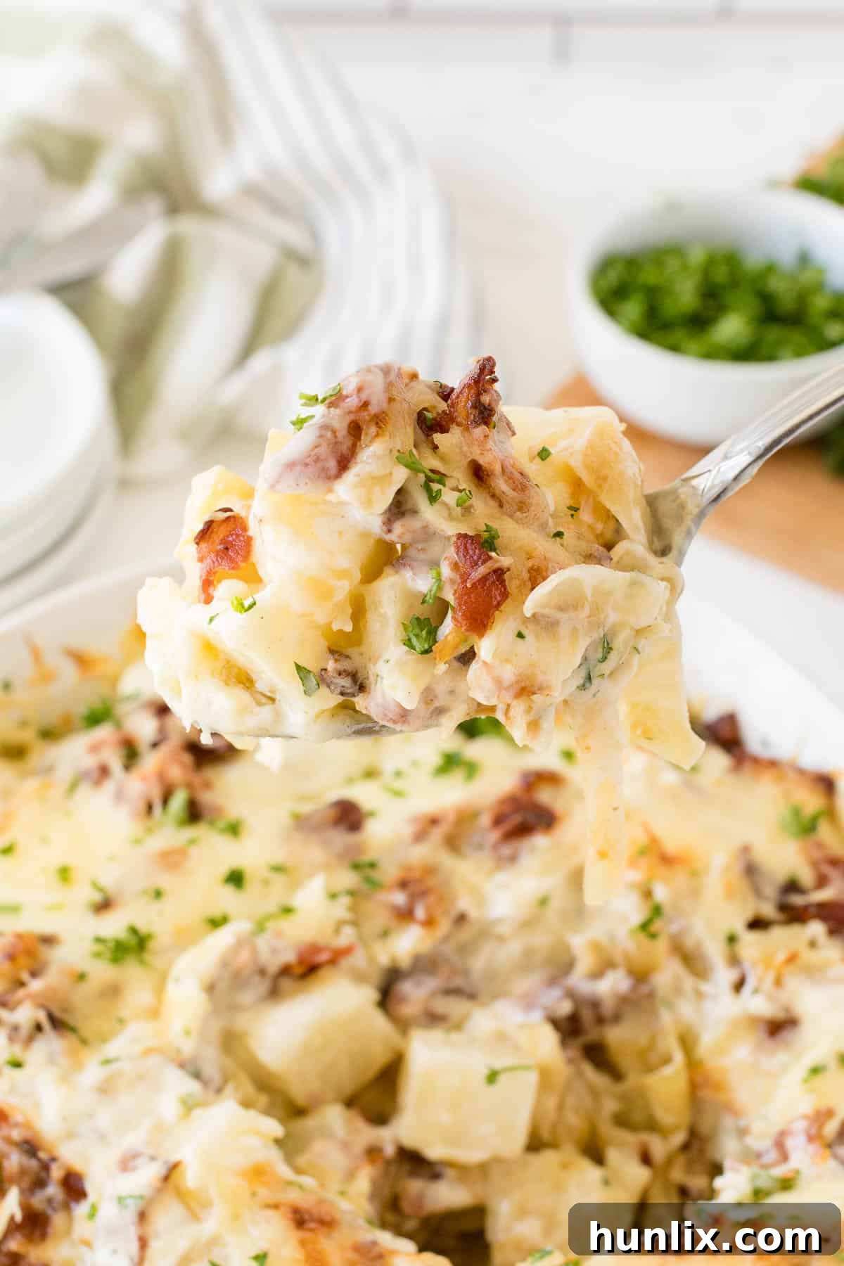 Crispy Bacon Ranch Potatoes 4 A close-up of a serving spoon scooping up Bacon Ranch Potatoes from a casserole dish, highlighting the layers.