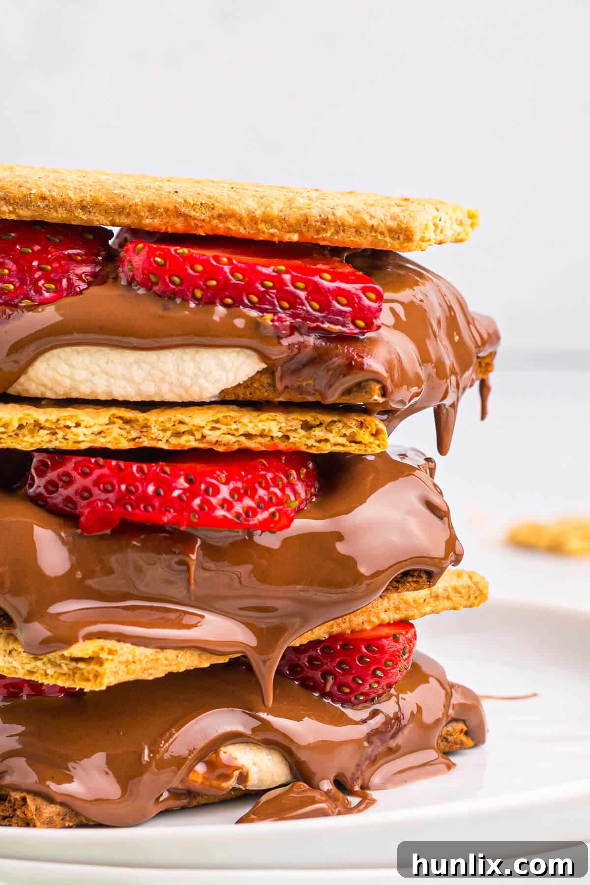 A stack of strawberry s'mores, showing a graham cracker base, melted chocolate, toasted marshmallow, and fresh strawberry slices.