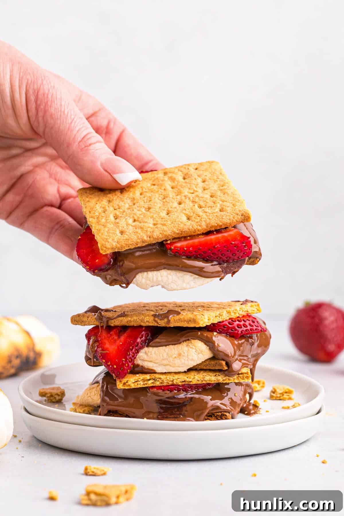 A hand holding a freshly made strawberry s'more, ready to be enjoyed.