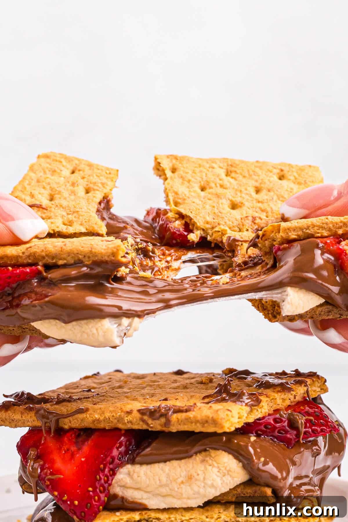 A hand breaking apart a warm, gooey strawberry s'more, showing the melted chocolate and marshmallow.