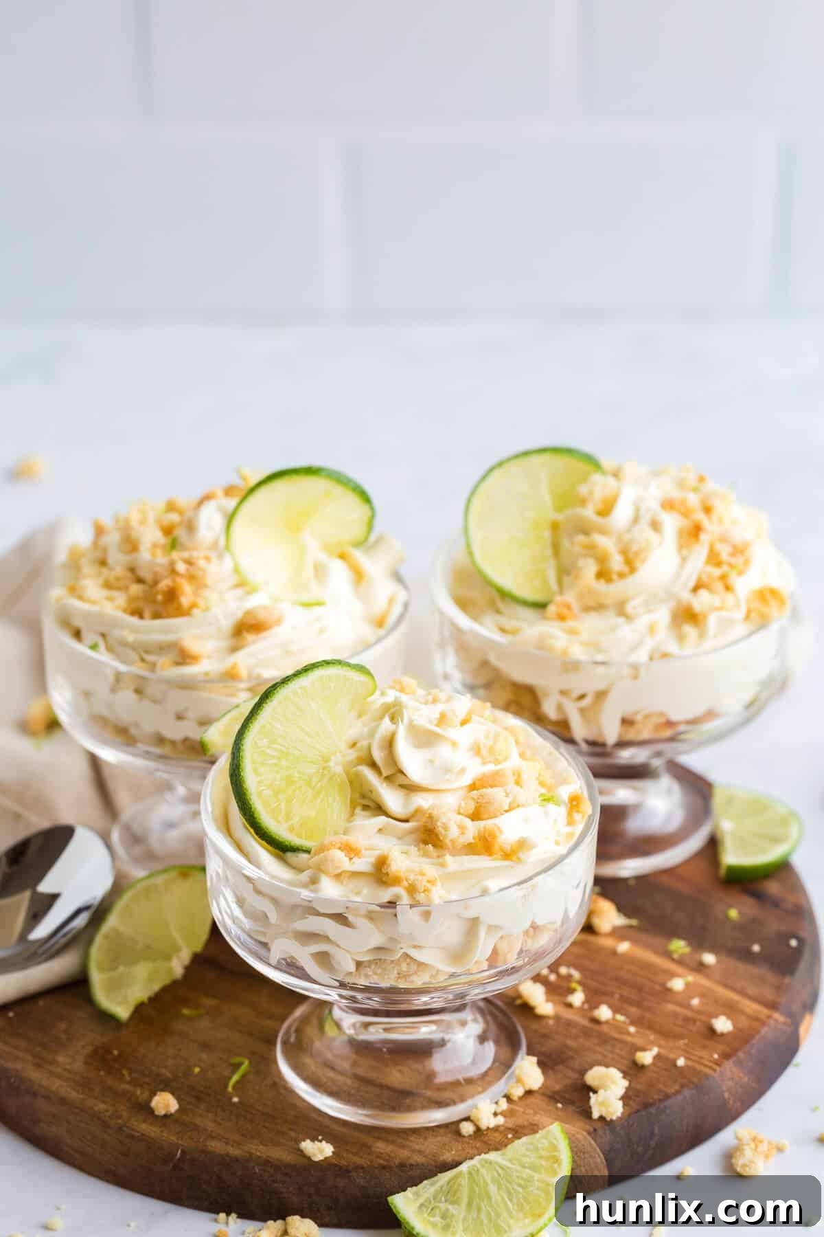 Three lime cheesecake parfaits on a wooden board, showcasing layers of golden cookie crust and creamy lime filling.