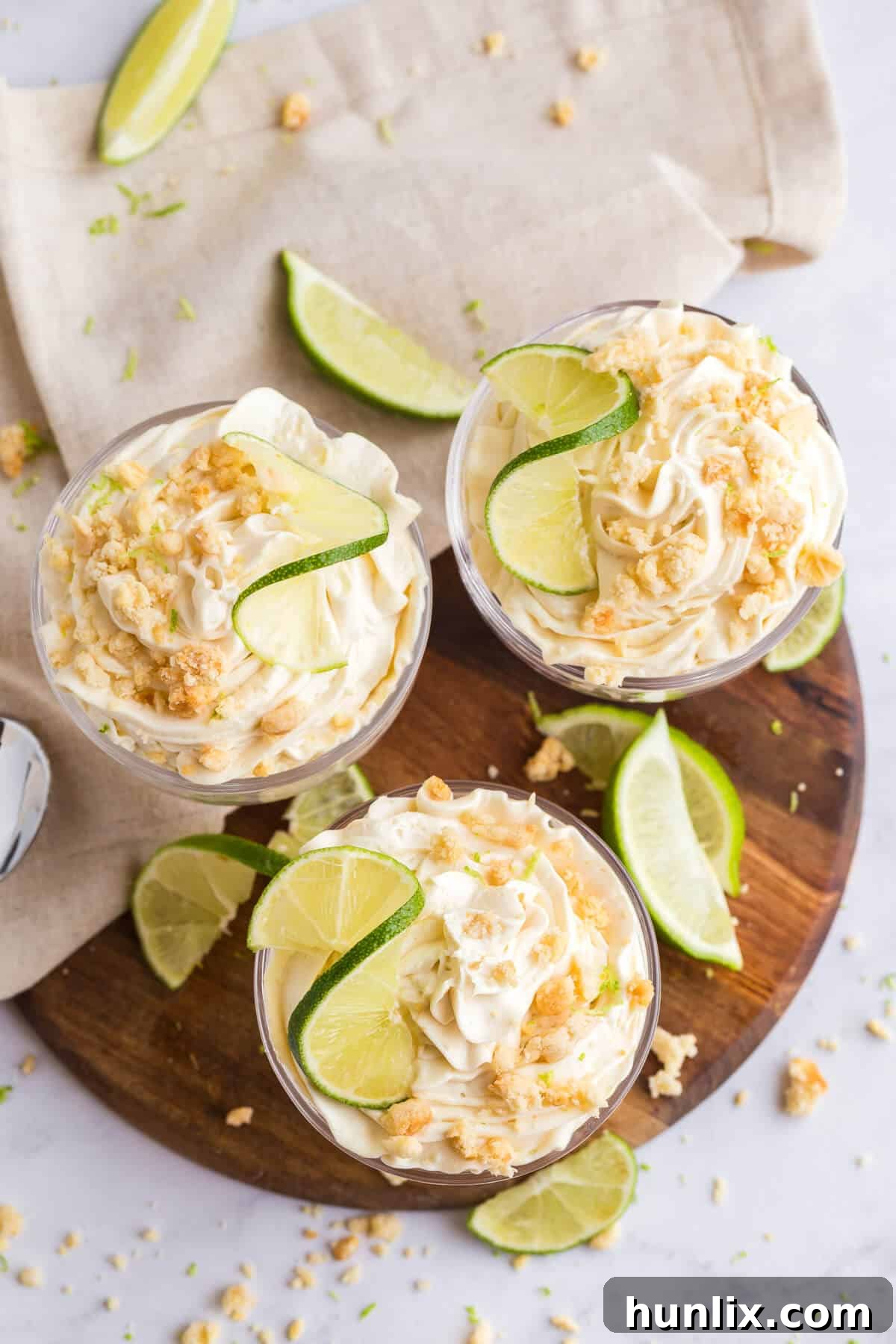 An overhead shot of three meticulously prepared lime cheesecake parfaits in glass dishes.