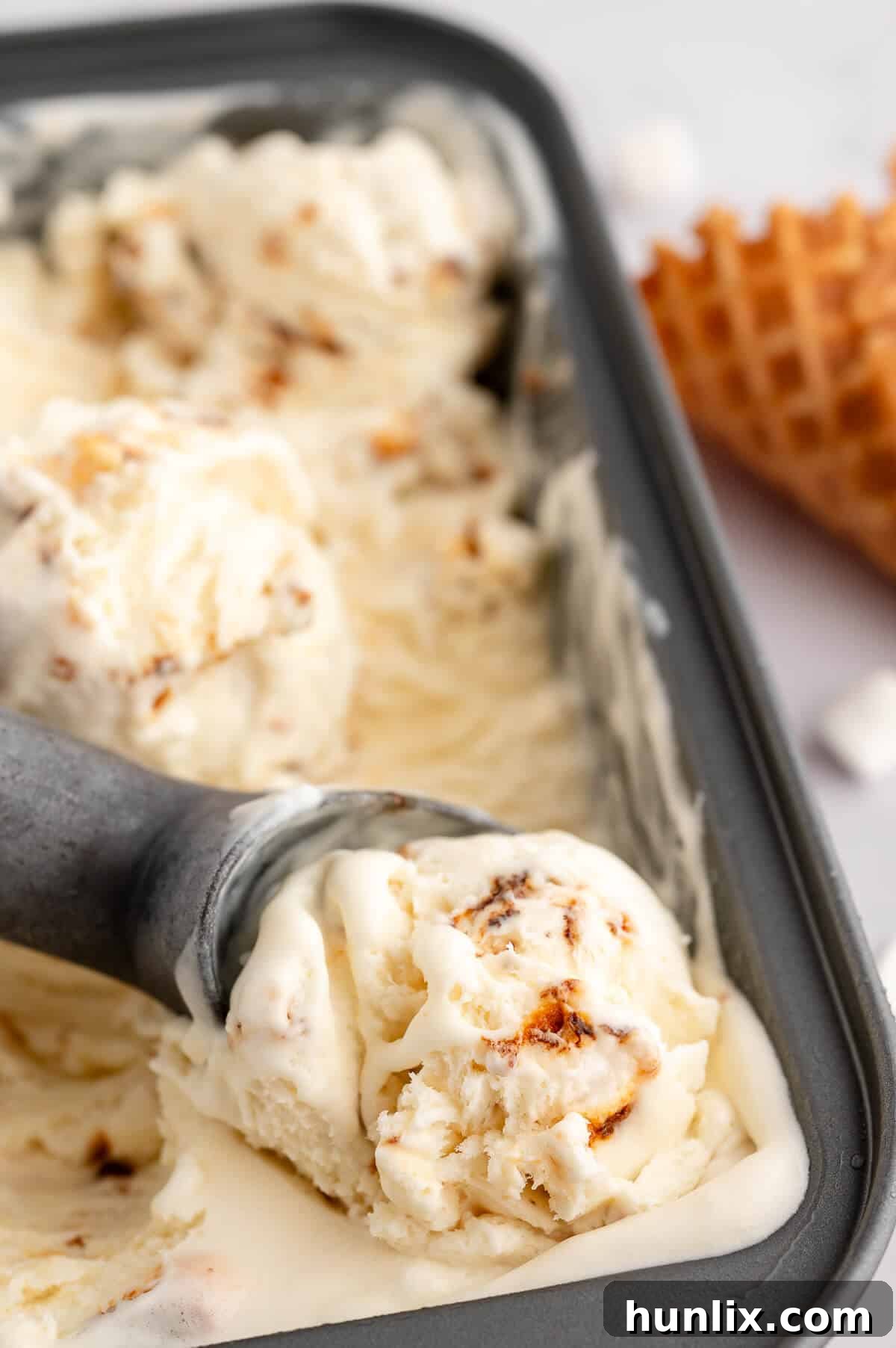A loaf pan of toasted marshmallow ice cream with an ice cream scoop, ready to be served.