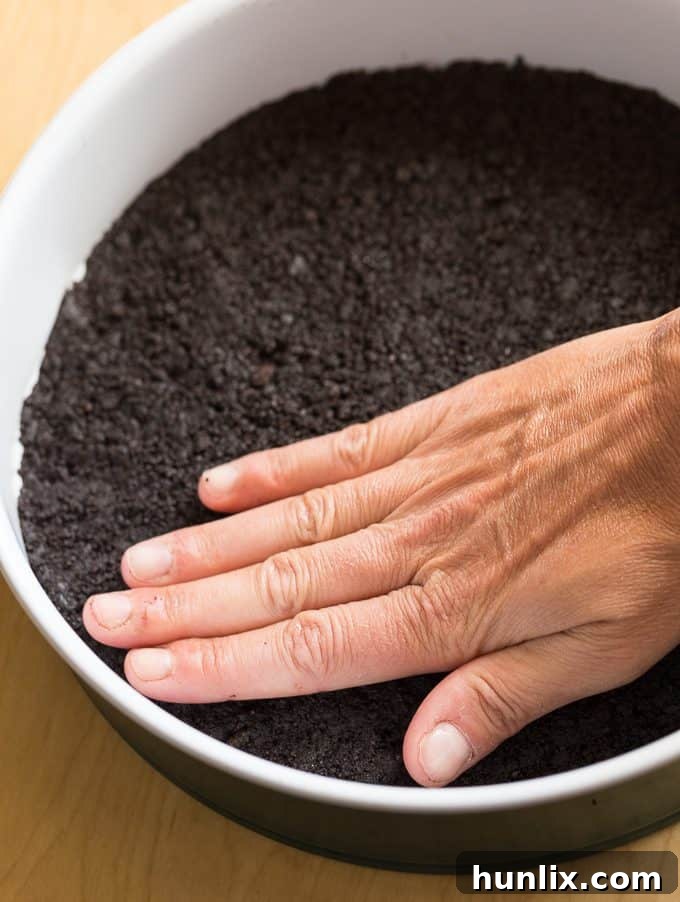 Pressing chocolate cookie crust into a 9-inch springform pan, preparing the base for a delicious Saint Lucian chocolate cheesecake.