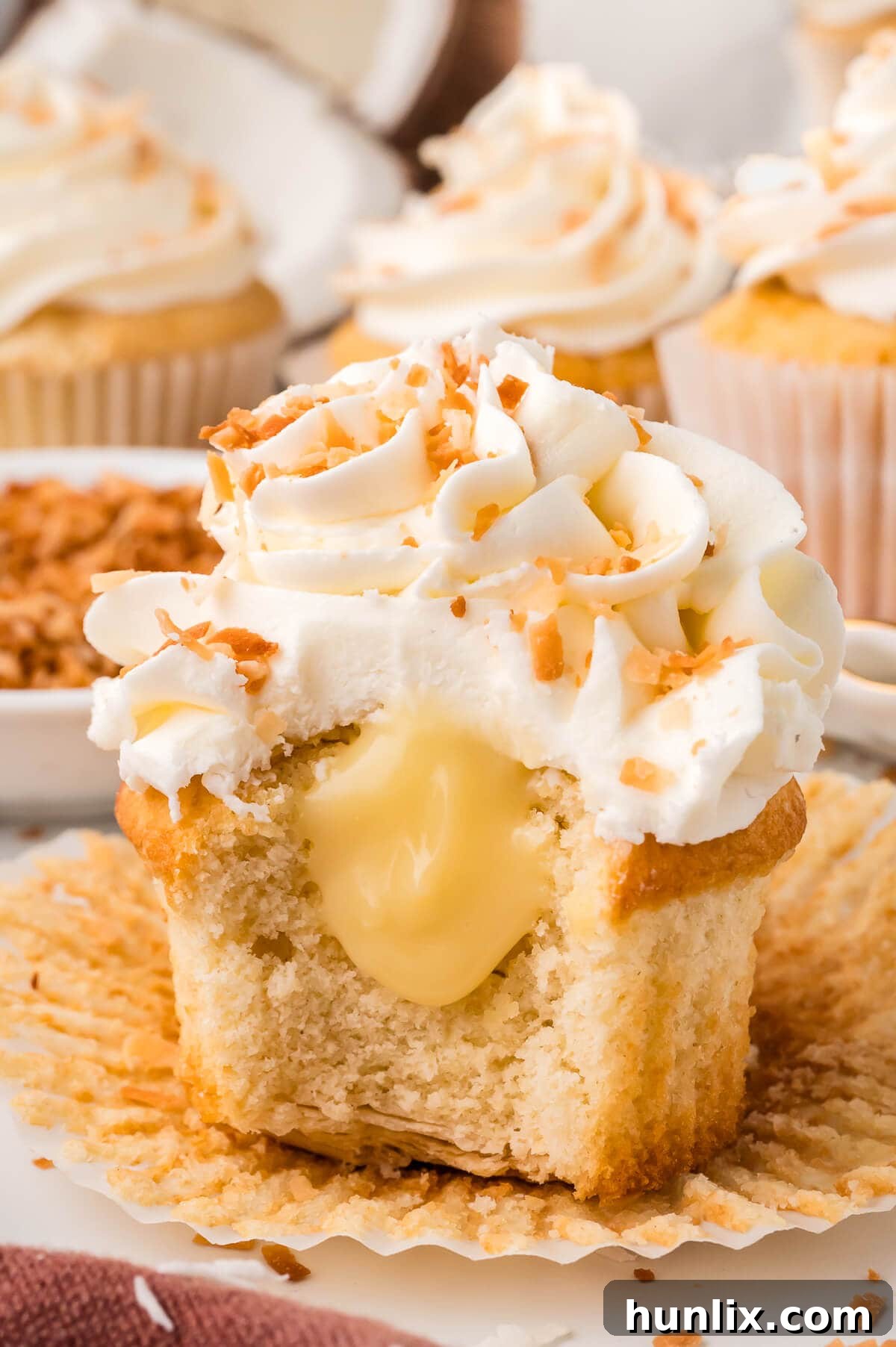 A perfectly sliced Coconut Cream Pie Cupcake revealing its golden crust, fluffy cake, and creamy coconut filling inside.