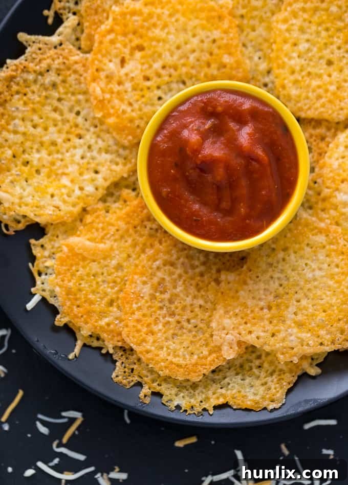 Crispy homemade cheese chips arranged artfully on a platter with a side of vibrant pizza sauce for dipping.