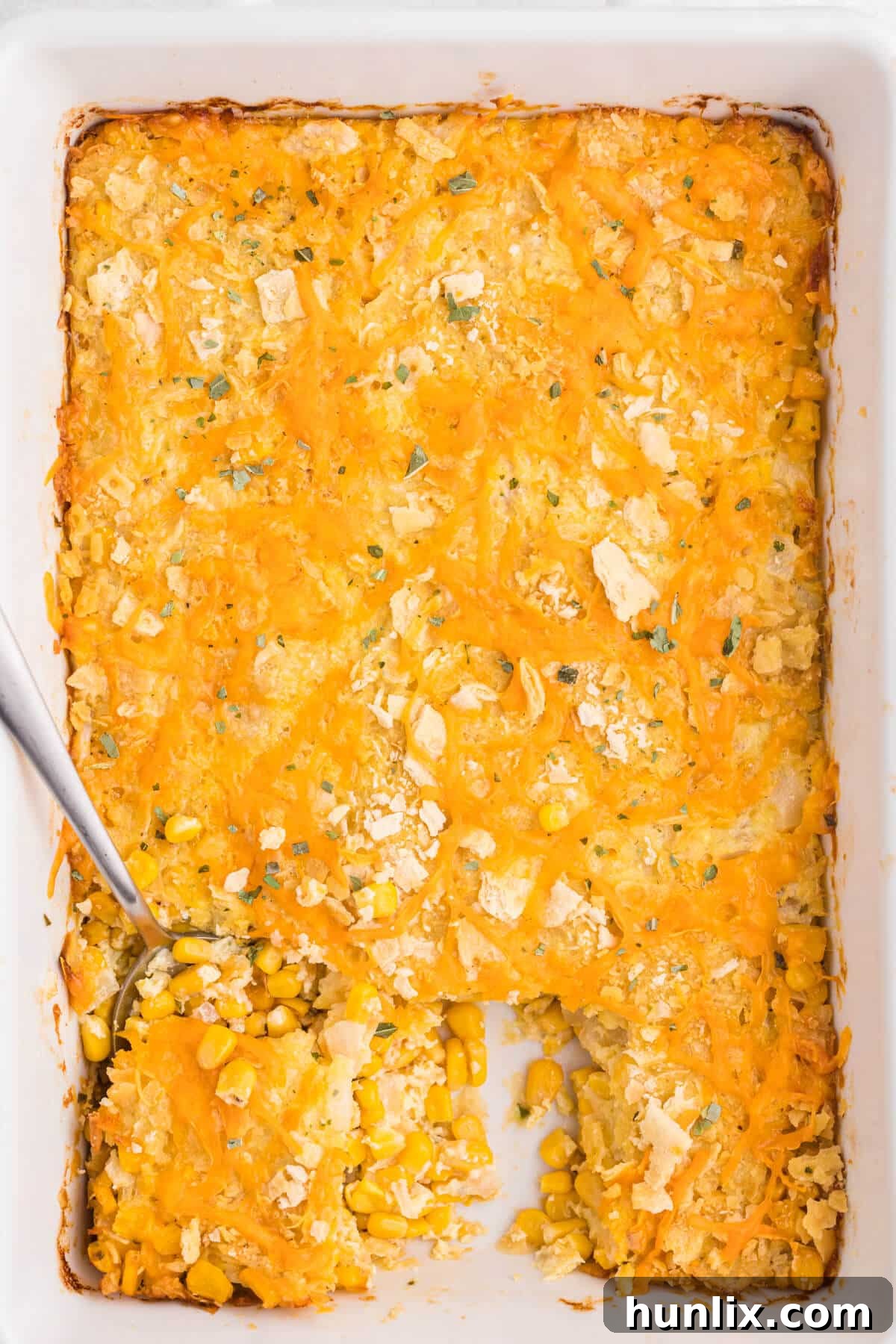 The finished cheesy corn casserole in a pan with a serving spoon.