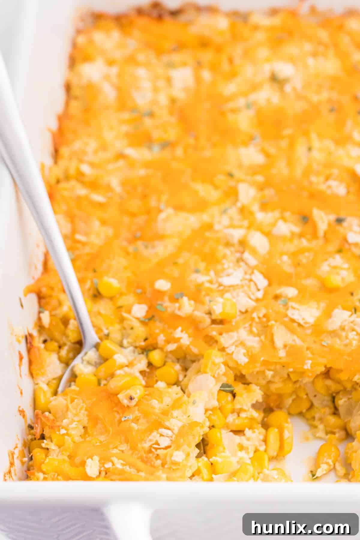 The finished cheesy corn casserole in a pan with a serving spoon, garnished with fresh basil.