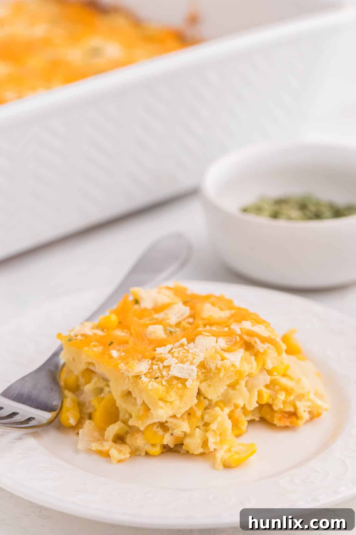 A perfectly portioned piece of cheesy corn casserole on a white plate with a fork.