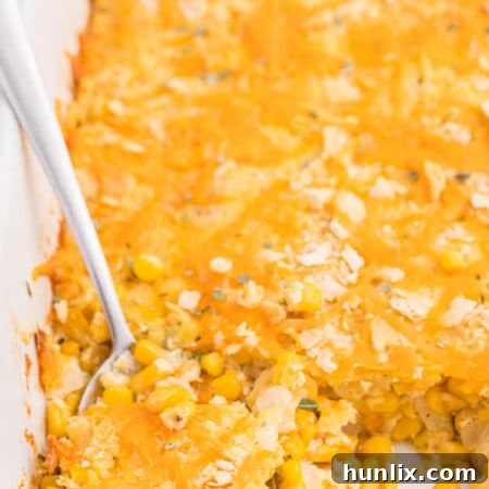 The finished cheesy corn casserole in a white casserole dish with a serving spoon.